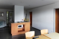 2 Stühle an Esstisch, dahinter zwei Kückenunterschränke in Bucheoptik mit Mikrowelle, grauer PVC-Boden.