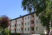 Wohnhaus drei Etagen, hellgelbe Fassade, Balkonbrüstungen orange, davor Grünfläche.