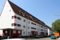 Altbauten mit Spitzdach, 4 Etagen, Vorgärten begrünt. Fassade weiß mit roten Akzenten. Straße.
