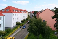 Straße mit Kopfsteinpflaster aus Dachwohnung gesehen. Lins Häuser hellblau, rechts Häuser orange, Bäume.
