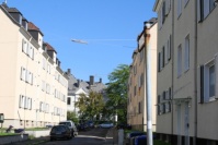 Schmale Straße mit hellen, sanierten Altbauten mit Klappläden, 4 Etagen. Parkende Autos.