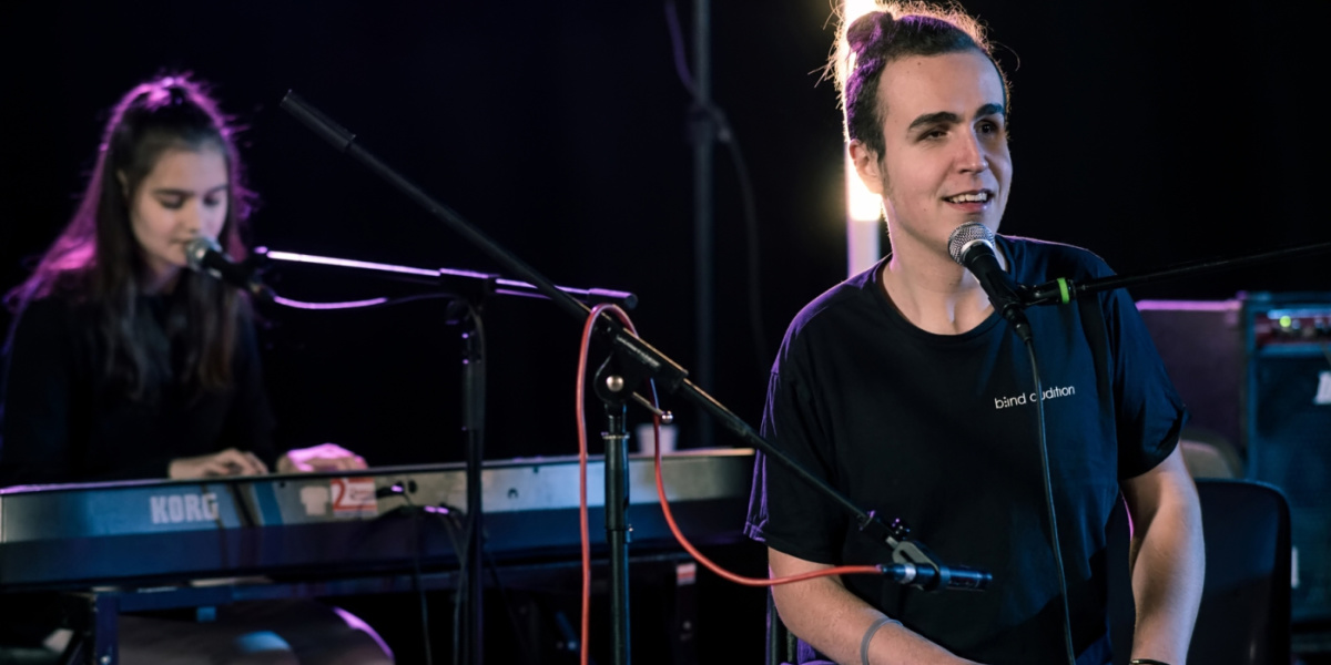 Mann in Rollstuhl singt, dahinter Frau am Klavier Mann in Rollstuhl singt, dahinter Frau am Klavier