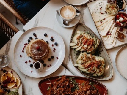 Eine Portion Pancakes mit Sahne und frischen Beeren sowie zwei Stullen mit unterschiedlichen Toppings, eine Käseplatte und ein Cappuccino 