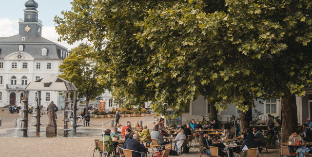 Außenansicht Café am Schloss: Tische unter großen Baum mit Blick auf das Alte Rathaus Saarbrücken