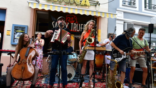 Eine Band mit acht MusikerInnen – unter anderem Cello, Akkordeon, Saxophon, Gitarre, Bass und Schlagzeug – vor der Kneipe Tante Anna