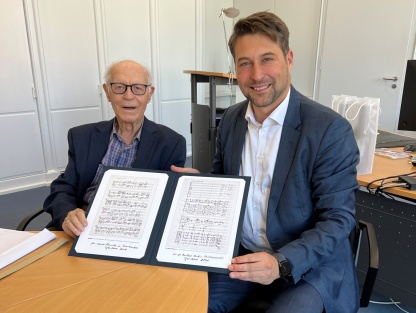 Zwei Personen sitzen aneinem Tisch und halten ein Buch in den Händen