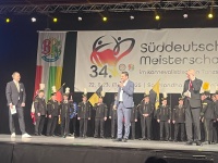 Mehrere Personen, teilweise in Uniform gekleidet, stehen auf einer Bühne. 