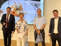 Drei Männer und eine Frau stehen im Saal