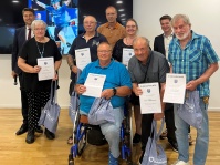 Eine Gruppe älterer Menschen mit ihren Ehrenurkunden, darunter ein Rollstuhlfahrer. Im Hintergrund stehen zwei Männer ohne Urkunde