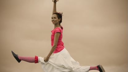 Frau macht in der Luft Spagat und hält Herz-Ballon in der Hand