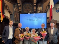 Viele ältere Personen sitzen in einem Festsaal und lauschen einer Rede