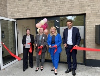 Vier Personen stehen vor einem Gebäude und zerschneiden ein Band um es einzuweihen