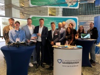 Eine Gruppe Menschen posiert an einem Messestand. Auf den Tischen vor der Gruppe liegen eine kleine Flugdrone und Prospekte aus