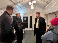 Drei Männer und eine Frau stehen in einem beleuchteten, großen Zelt und unterhalten sich