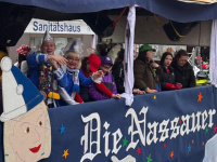 Mehrere kostümierte Personen stehen auf einem Umzugswagen mit der Aufschrift „Die Nassauer“ und schauen in Richtung Publikum.