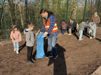 Erwachsener mit Warnweste hält blauen Müllsack, mehrere Kinder mit Stöcken und Müllsäcken sammeln Müll auf