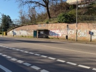 Straße mit Buswartehäuschen vor einer mit Graffiti besprühten Mauer