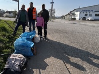 Vier Personen stehen neben mehreren blauen Müllsäcken, mit Industriegebäuden im Hintergrund