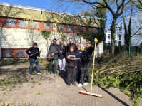 Gruppe von Menschen mit Gartengeräten und Besen vor einem Gebäude im Freien